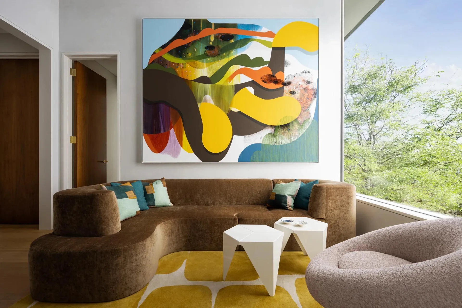 A modern living room with a curved couch, colorful abstract painting, and geometric coffee tables.