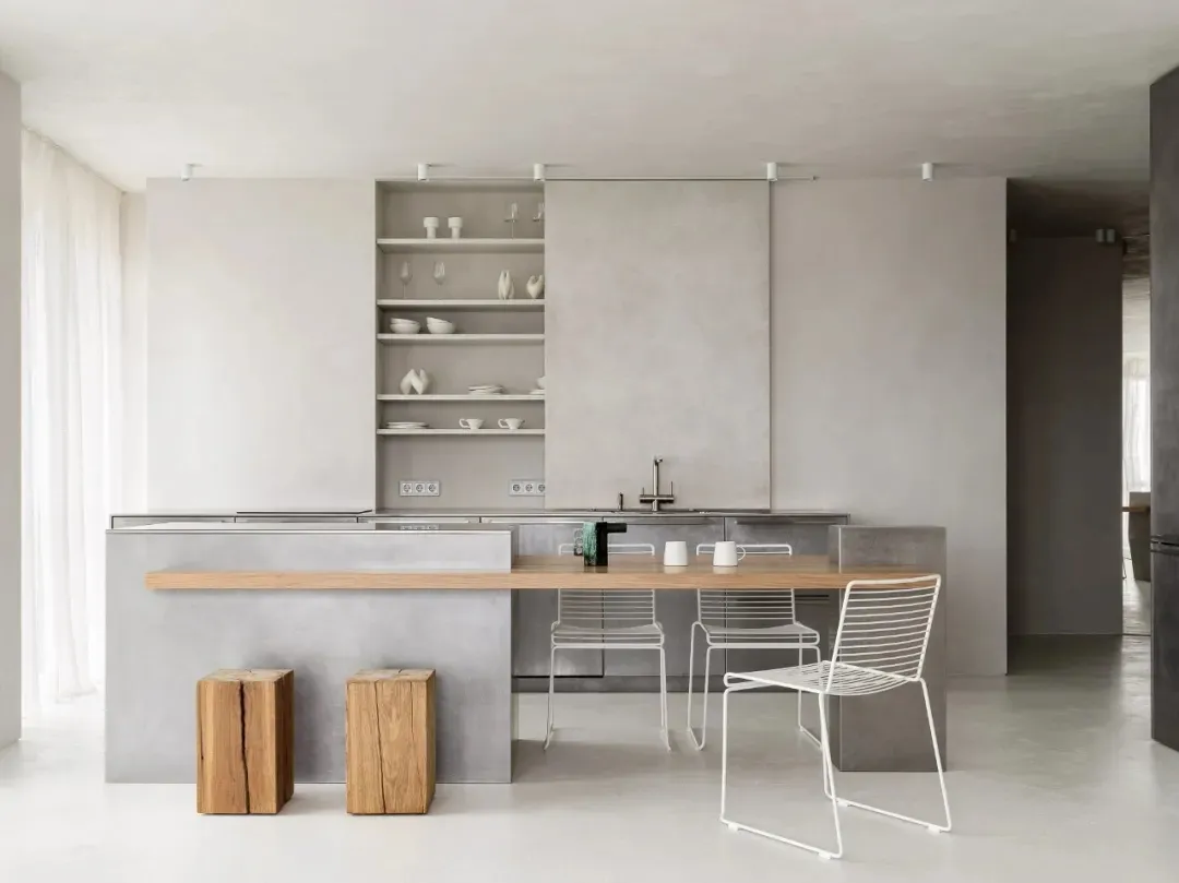 A modern minimalist kitchen features a concrete island and white cabinets with a clean, uncluttered design.