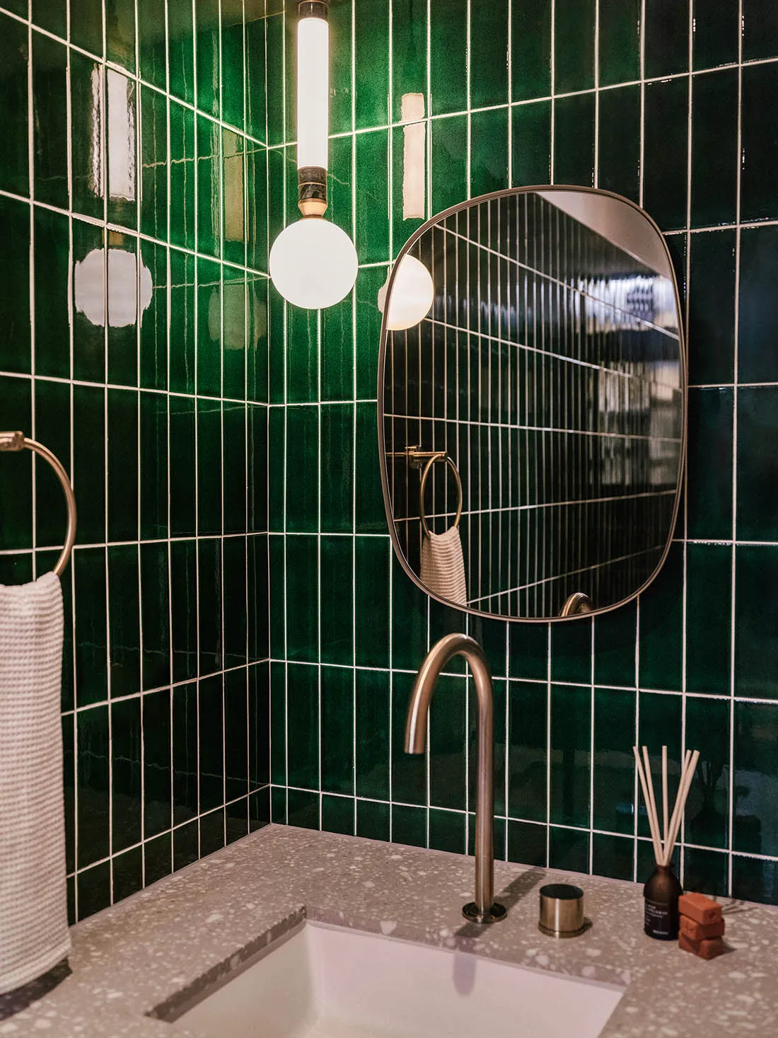 A modern bathroom with green tiles, a terrazzo countertop, and a round mirror.