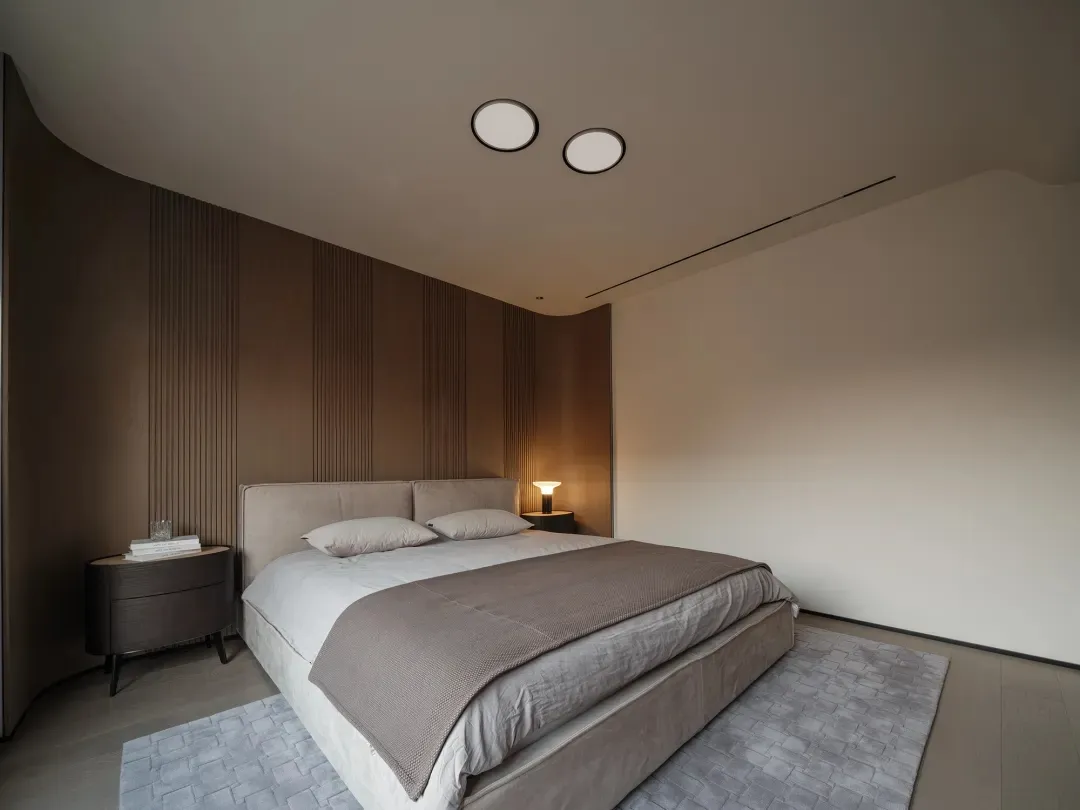 A minimalist bedroom with a bed featuring a herringbone pattern blanket, wooden floor, and a small nightstand with a single l