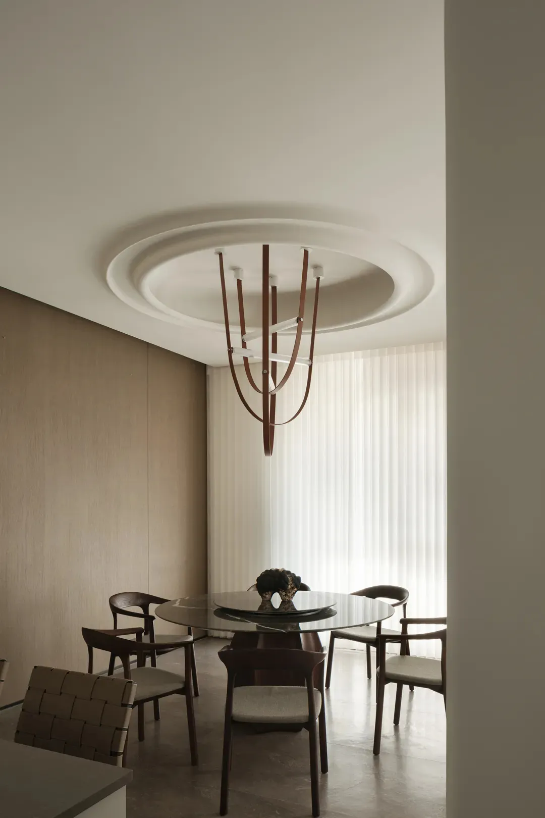 A minimalist dining room with a round glass table, wooden chairs, and a modern chandelier.