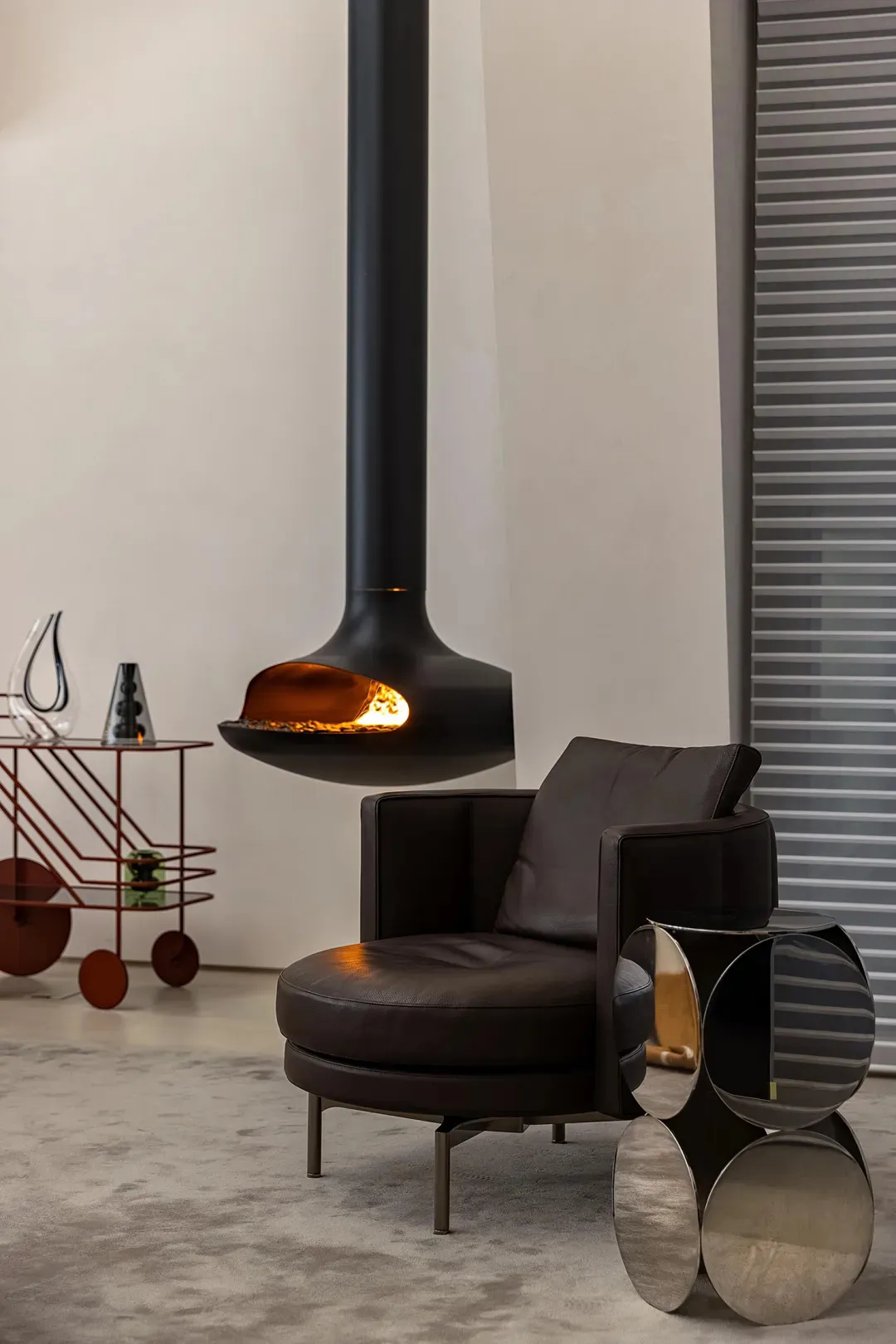 A modern living room featuring a black leather armchair, a metal coffee table, and a concrete floor, with a hanging fireplace