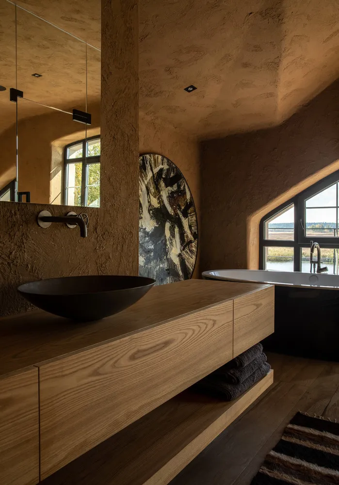 Modern minimalist bathroom featuring a wood vanity with a black bowl sink and a ceramic bathtub.