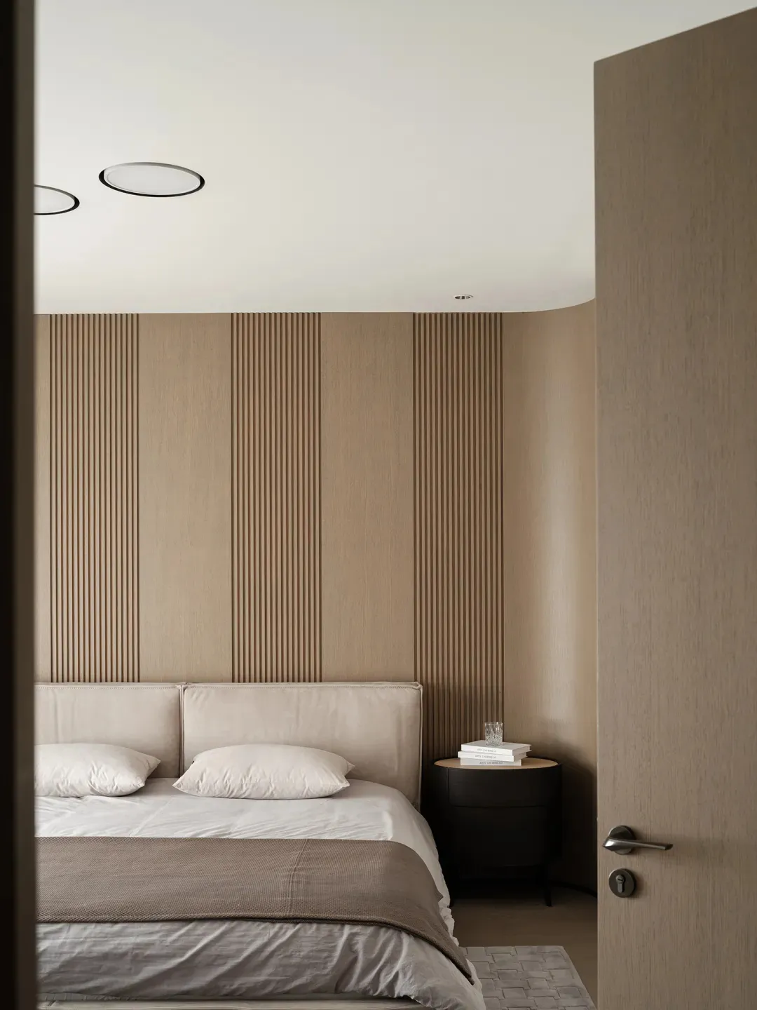 A minimalist bedroom with a bed, pillows, and a nightstand with a glass and books.