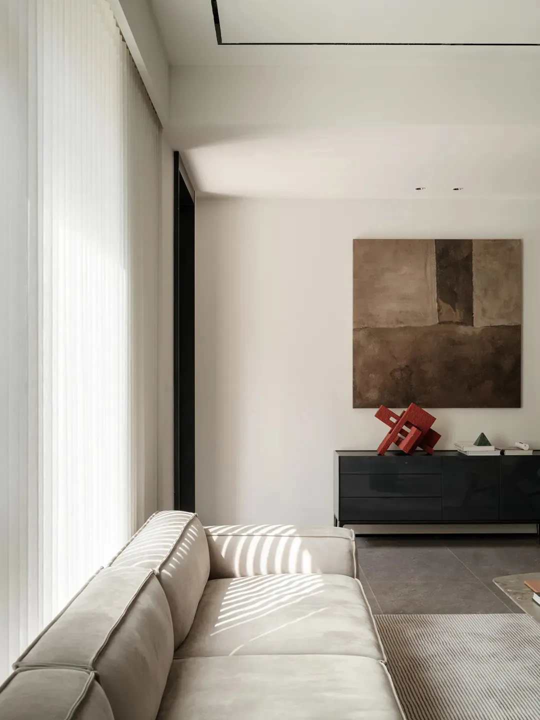 Minimalist living room with modern, neutral-colored sofa, concrete accent wall, and abstract artwork.