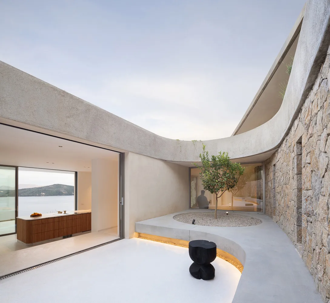 A modern penthouse patio featuring a circular concrete seating area with a small tree and a black stool, overlooking a scenic