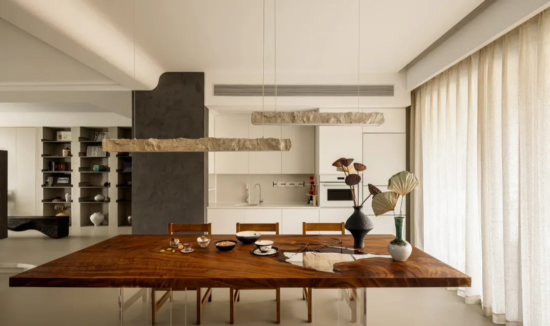 A modern residential kitchen with a wooden dining table and chairs, featuring a minimalist design with white cabinetry and a