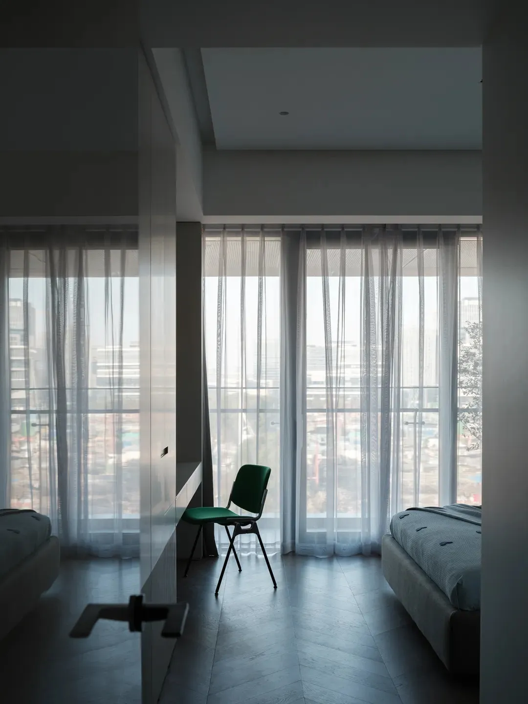 Minimalist bedroom featuring transparent fabric curtains and a green chair.
