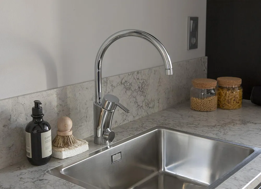 Modern kitchen featuring a stainless steel sink with a curved faucet, mounted on a marble countertop with jars of grains.