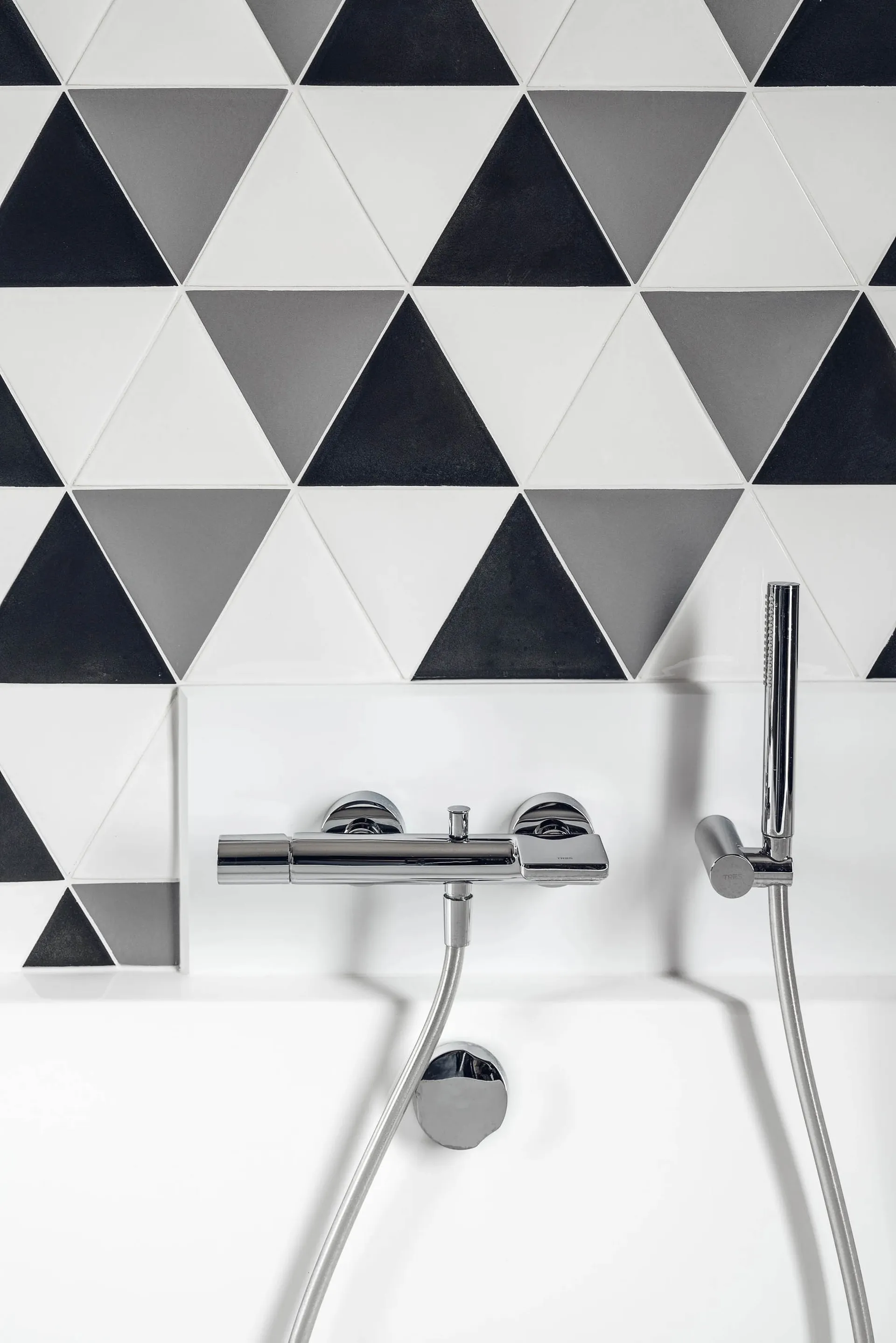 Modern minimalist bathroom with black, white, and gray geometric triangle ceramic tiles, featuring a chrome faucet and hand s