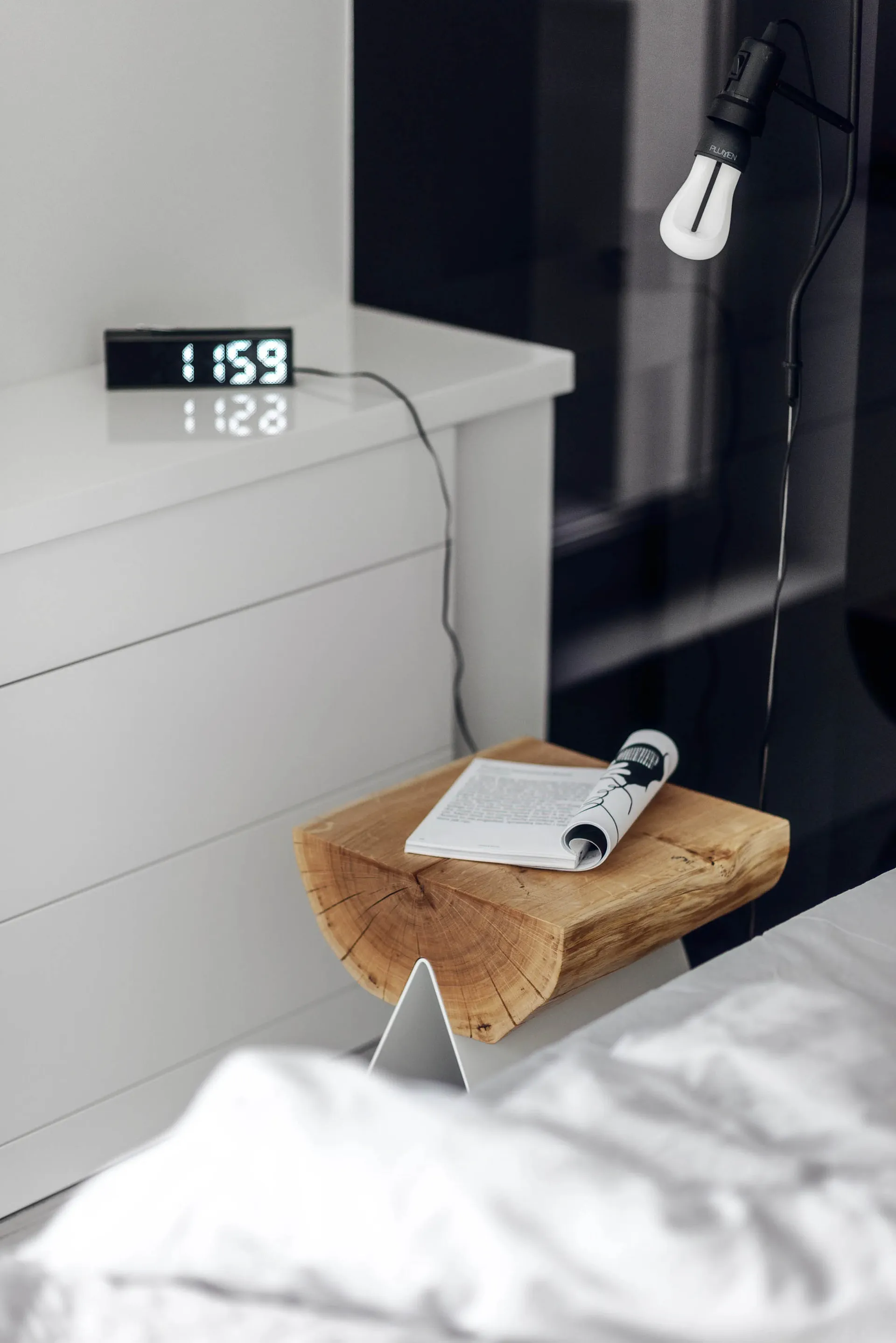 Minimalist bedroom featuring a wooden stool and metallic bedside lamp.