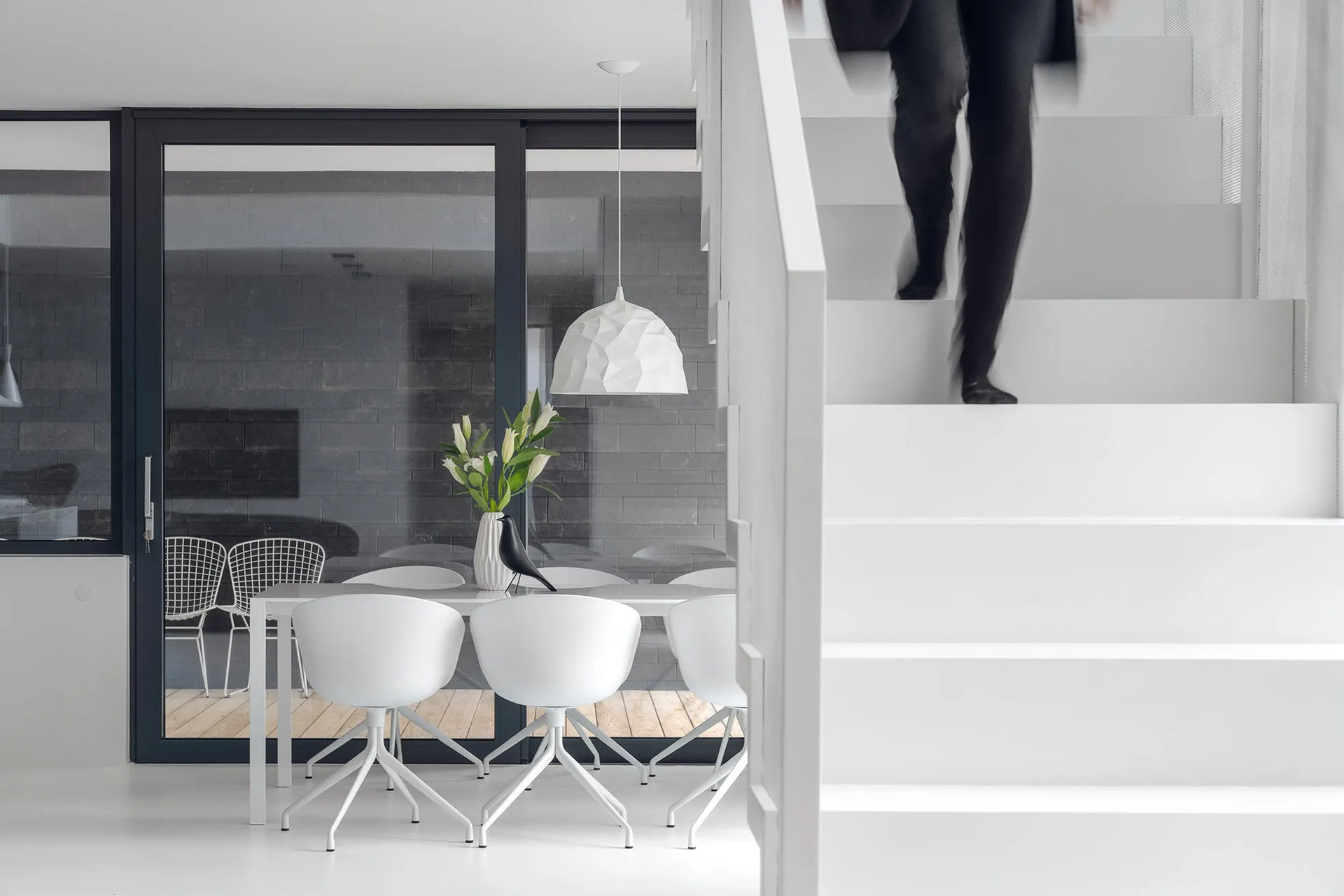 Modern minimalist staircase with concrete steps and a dining area with white chairs and a geometric pendant light.