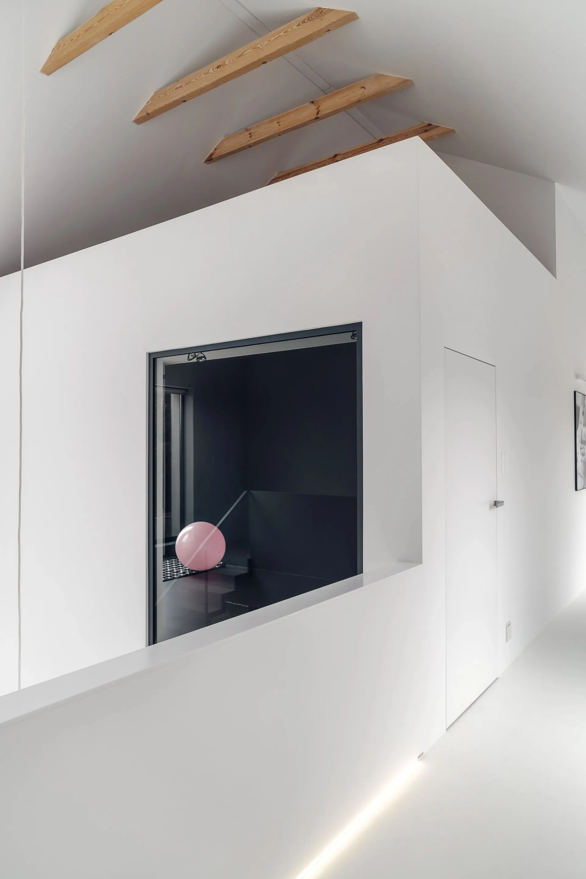 A white minimalist interior with a large window and wooden beams on the ceiling.