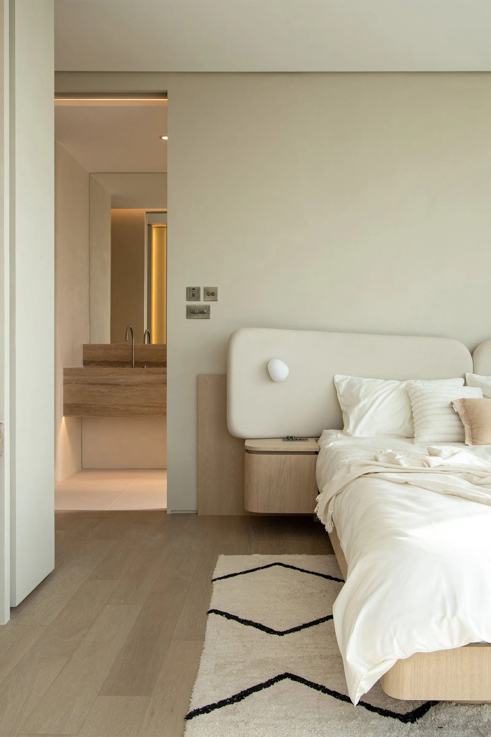 A minimalist bedroom with a white bed and wooden flooring.