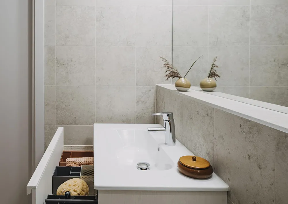 A modern bathroom with concrete walls, minimalist design, and a sleek white sink with a faucet. Decorative vases and a wooden