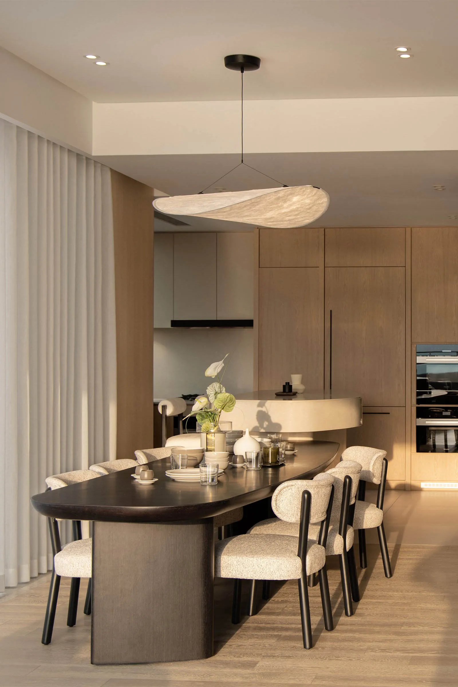 An elegantly designed dining room featuring a modern wooden table with upholstered chairs and a minimalist light fixture abov