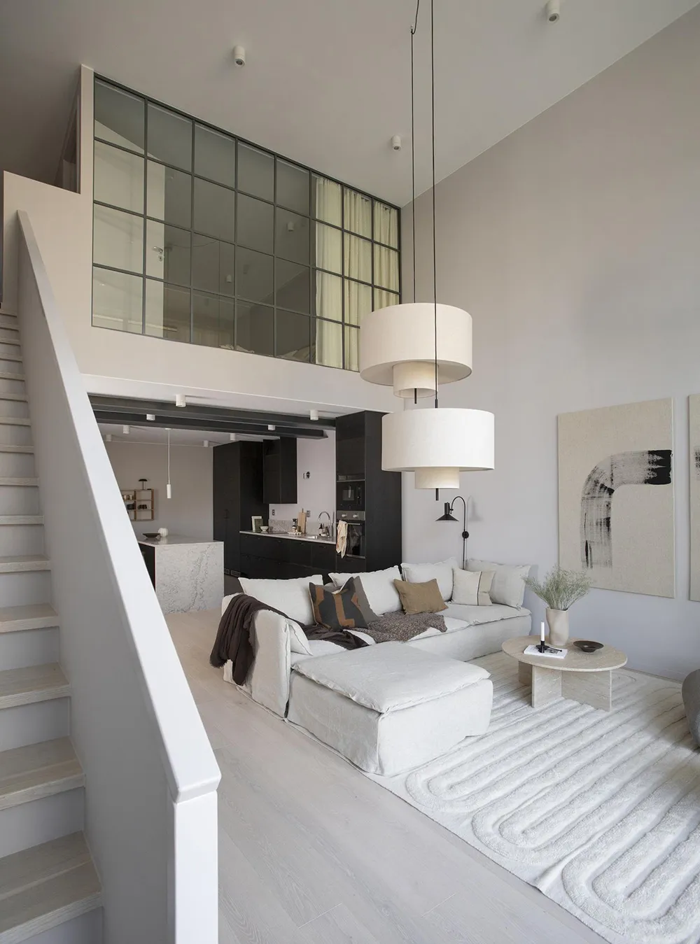 A modern minimalist living room with neutral-toned furniture and decor, featuring a large sectional sofa, a round coffee tabl