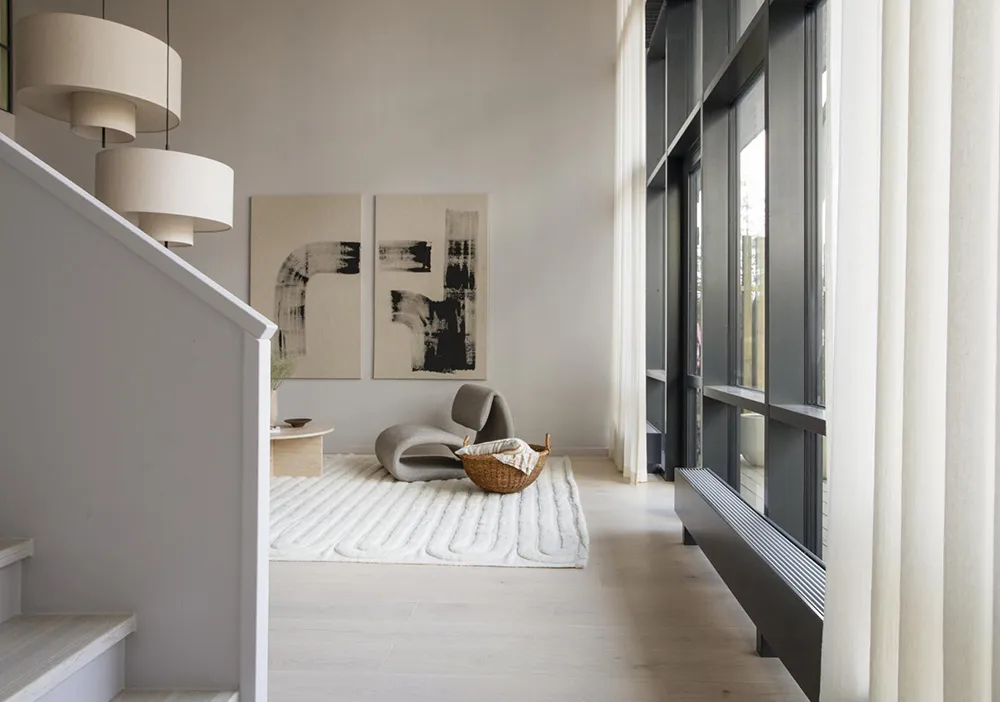A modern, neutral-toned living room with minimalist decor, light-colored wood floors, and large windows.