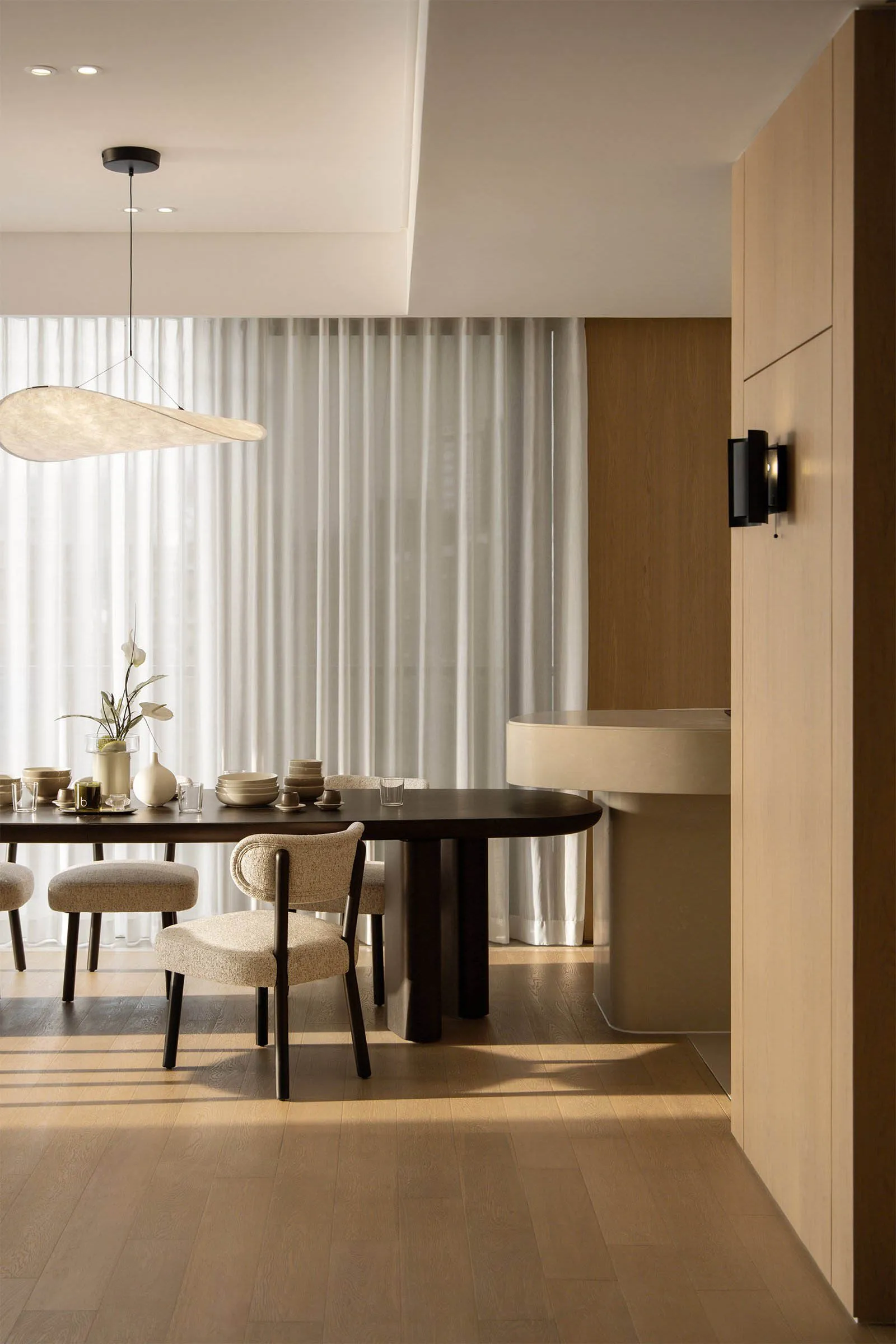 A modern residential interior featuring a wooden dining area with a round table and minimalist furniture, overlooking a citys