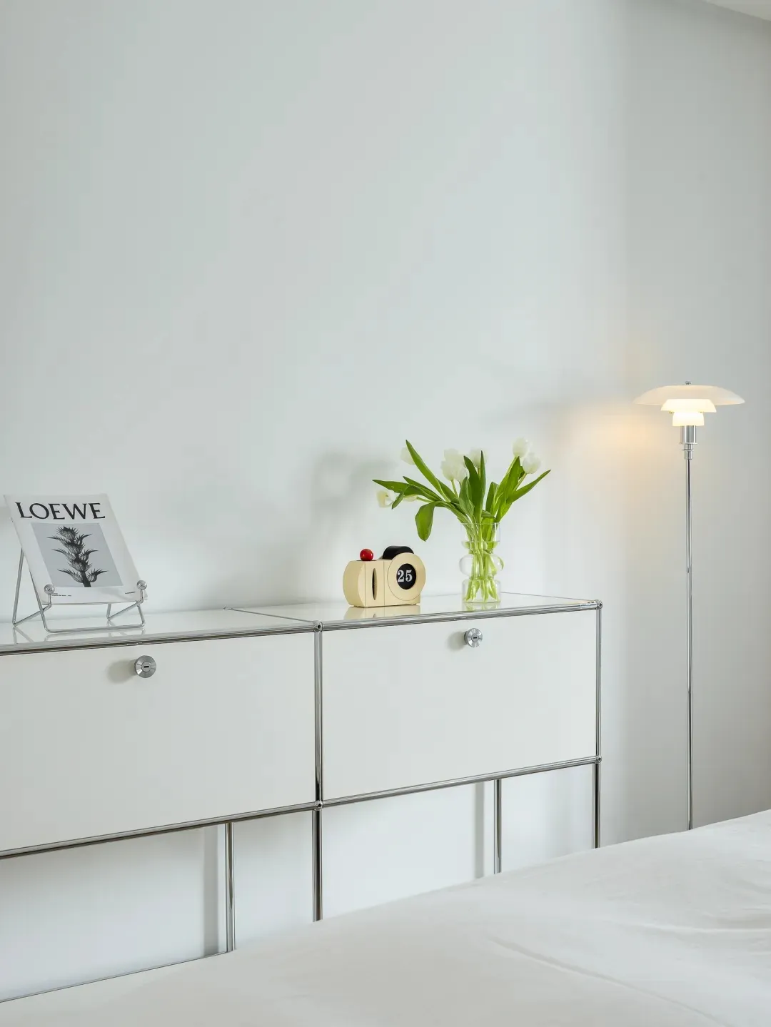 A minimalist bedroom featuring a glass cabinet, white tulips, and a floor lamp.
