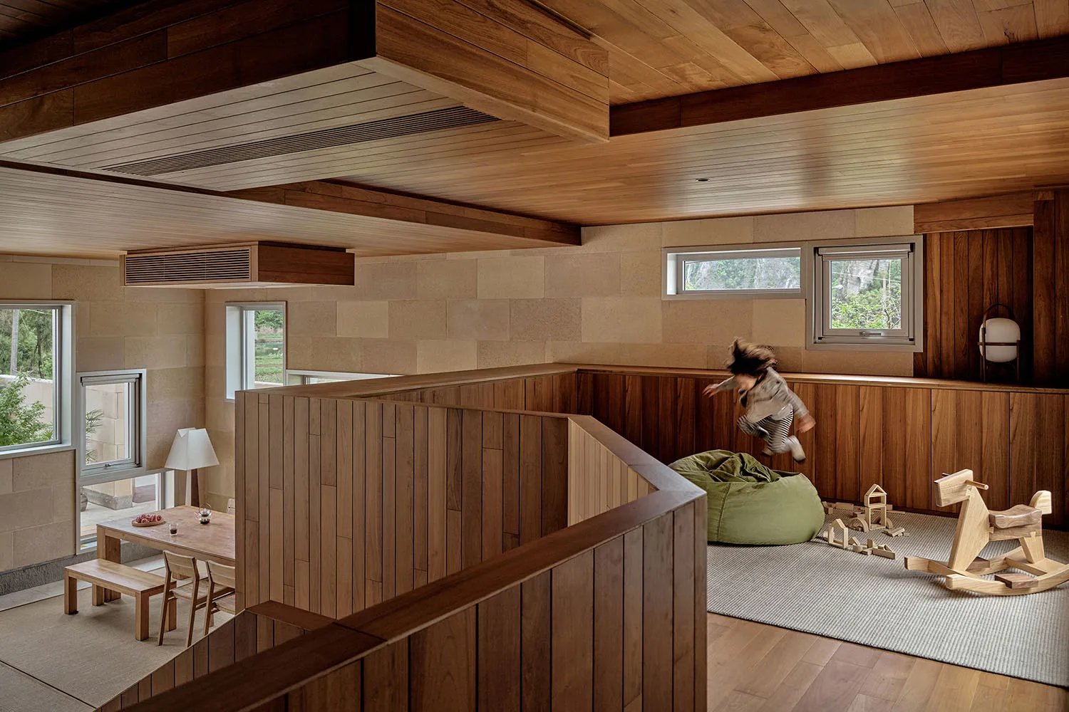 A modern playroom with wooden walls and flooring, featuring a child jumping on a bean bag.