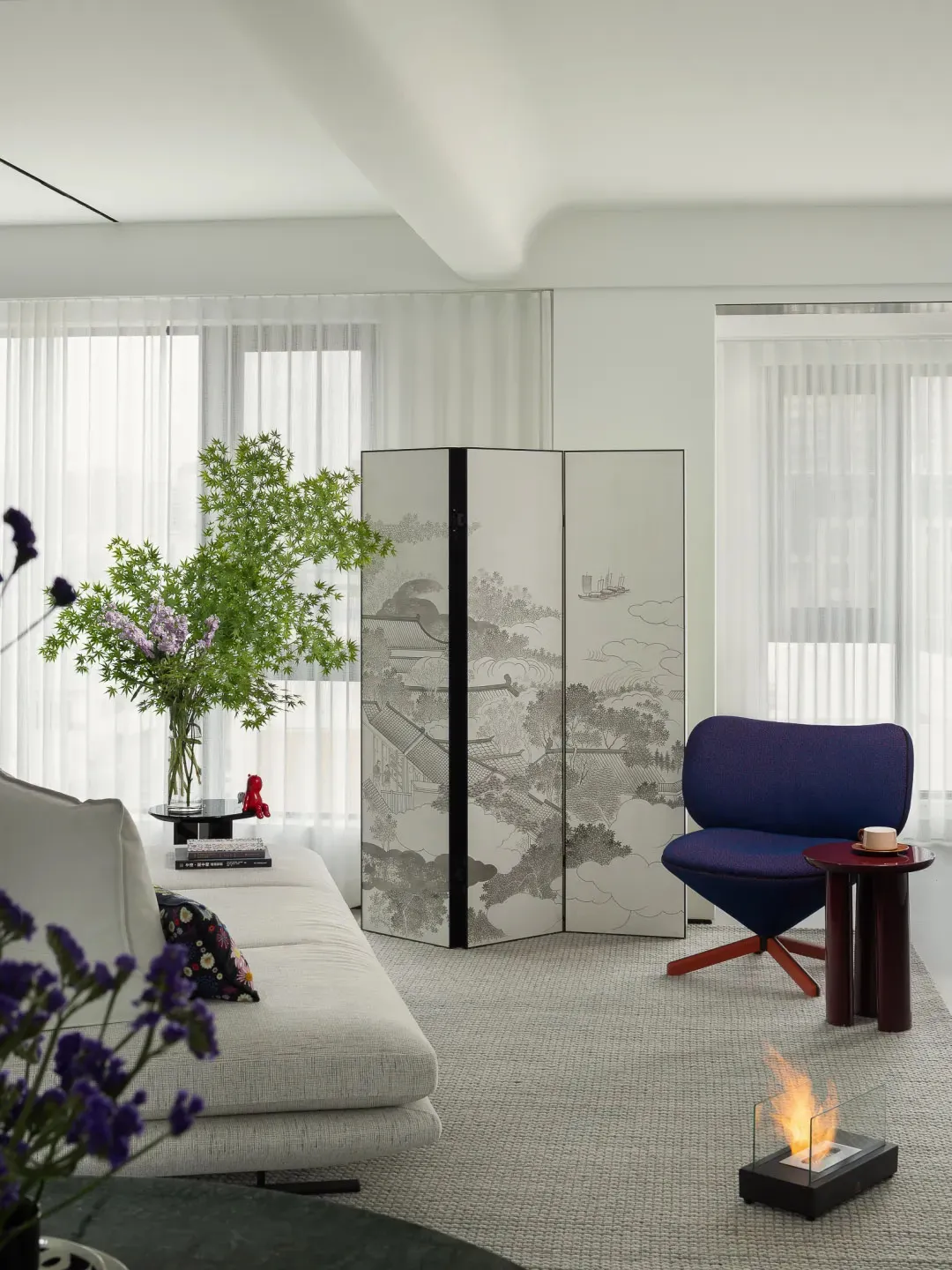 A minimalist living room with a modern decor featuring a white sofa, a purple armchair, a decorative partition, and a glass f