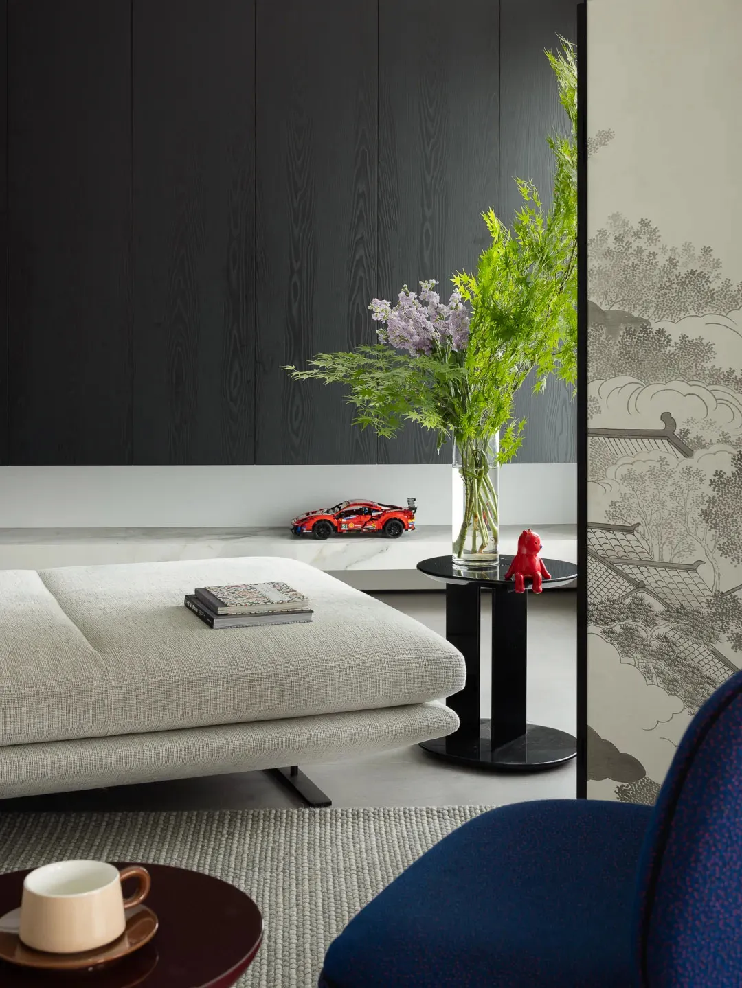 A modern living room featuring a minimalist design with textured fabric furniture, marble flooring, and a flower arrangement