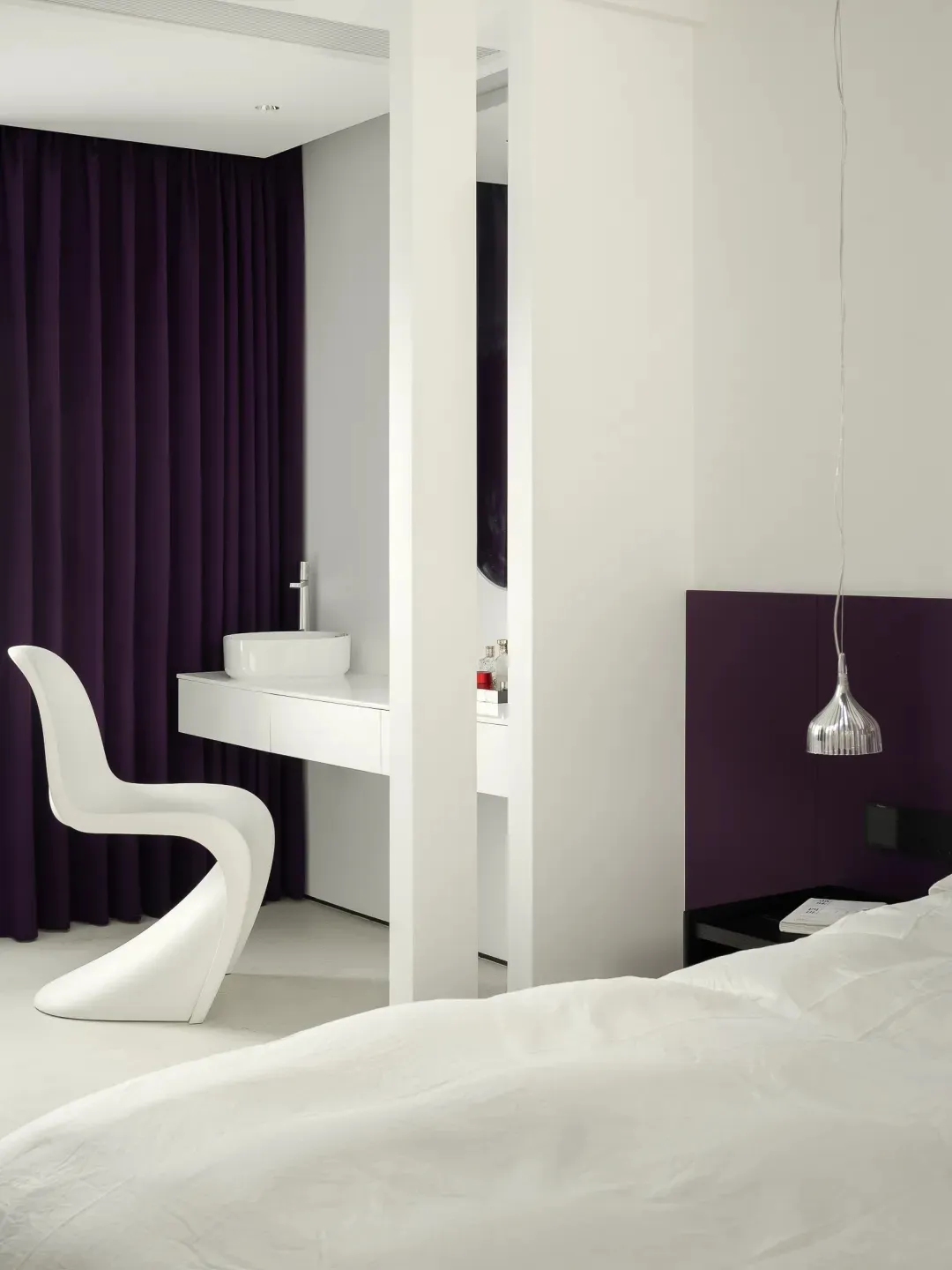 A modern bedroom with white wood flooring, purple accents, and a sleek, white chair.