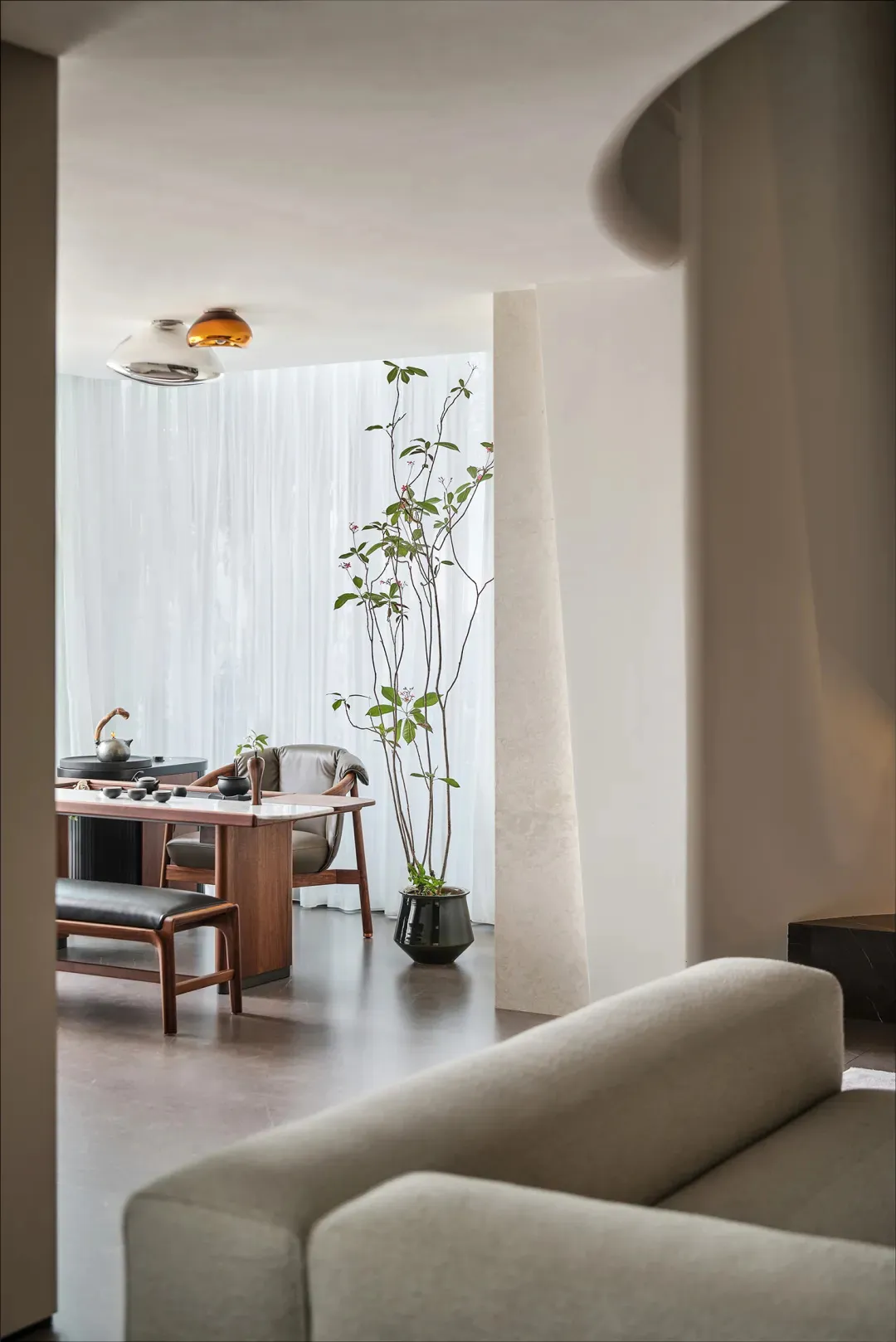 The minimalist living room features a concrete floor and sofa, along with a dining area with a wooden table and chairs.