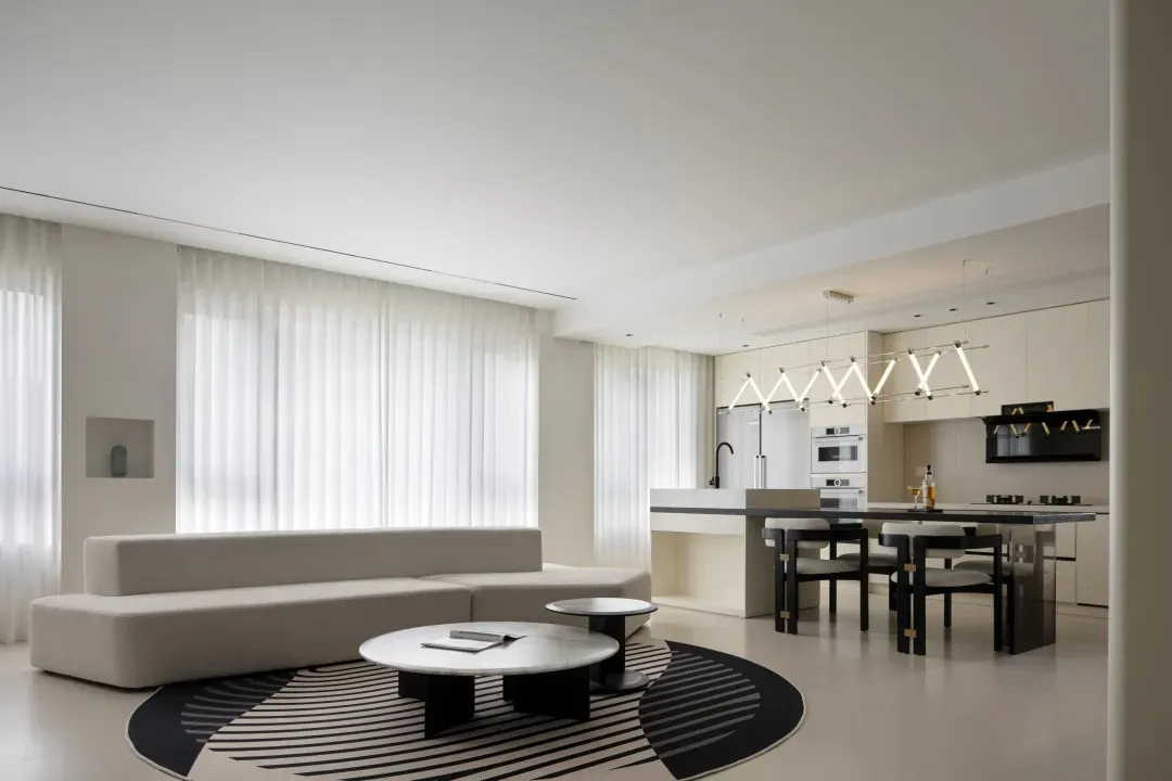 Modern, minimalist living room with a neutral color palette, featuring a white sectional sofa, round tables, and a geometric