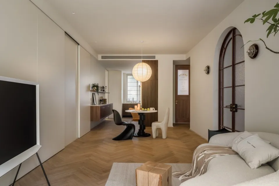 A modern living room with light wood flooring, a white sofa, and a minimalist design. Includes a dining area with a round tab