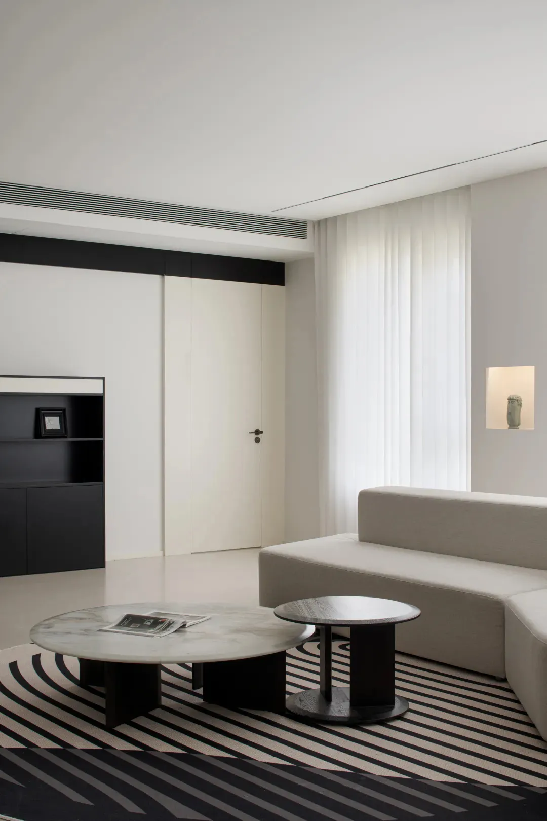 A modern minimalist living room with a black and white color scheme, featuring a white sofa, round marble tables, and a geome