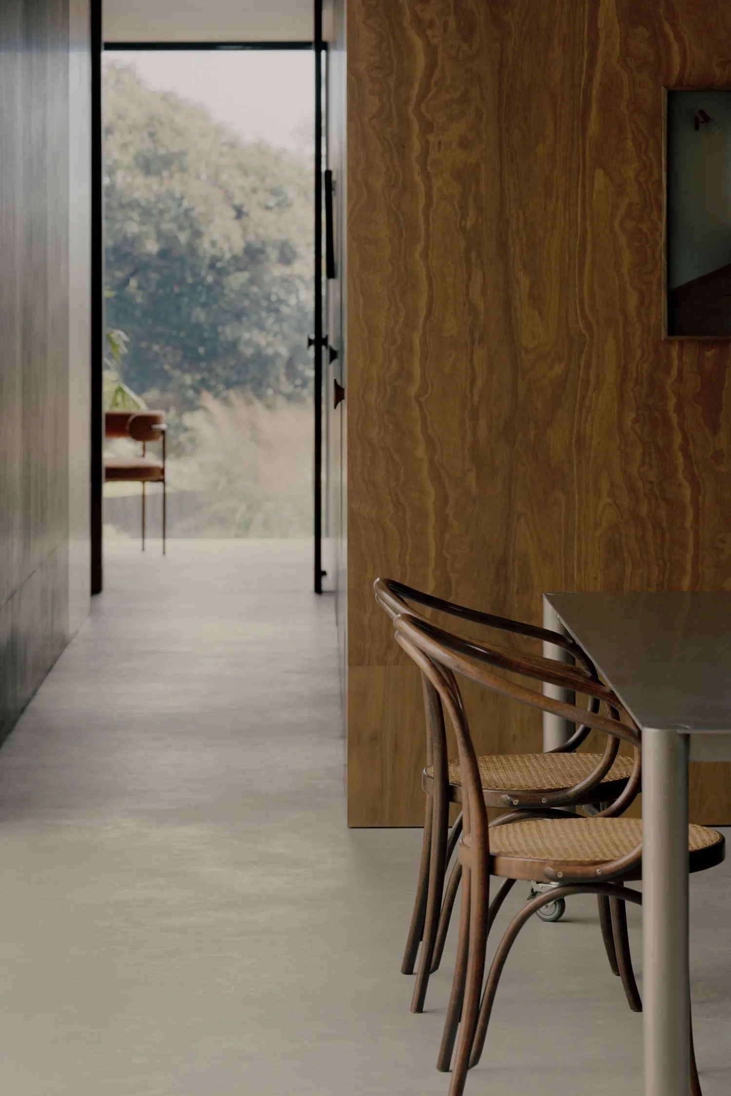 Modern dining room featuring a wooden wall and a steel table with wooden chairs.