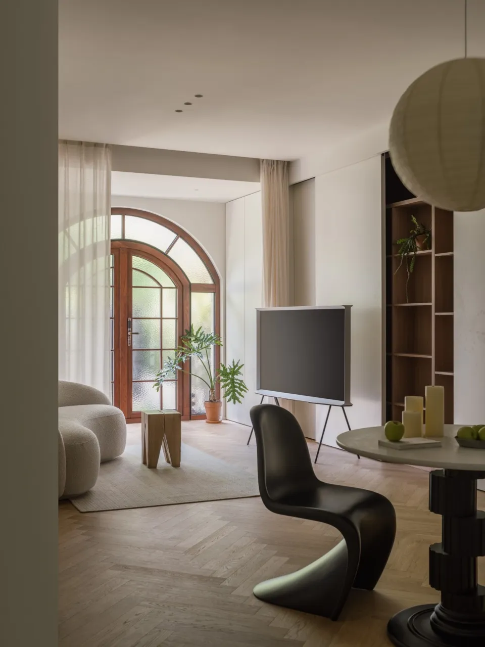 A modern living room featuring wooden flooring, a black curved chair, a round table with green apples, and a curved door with