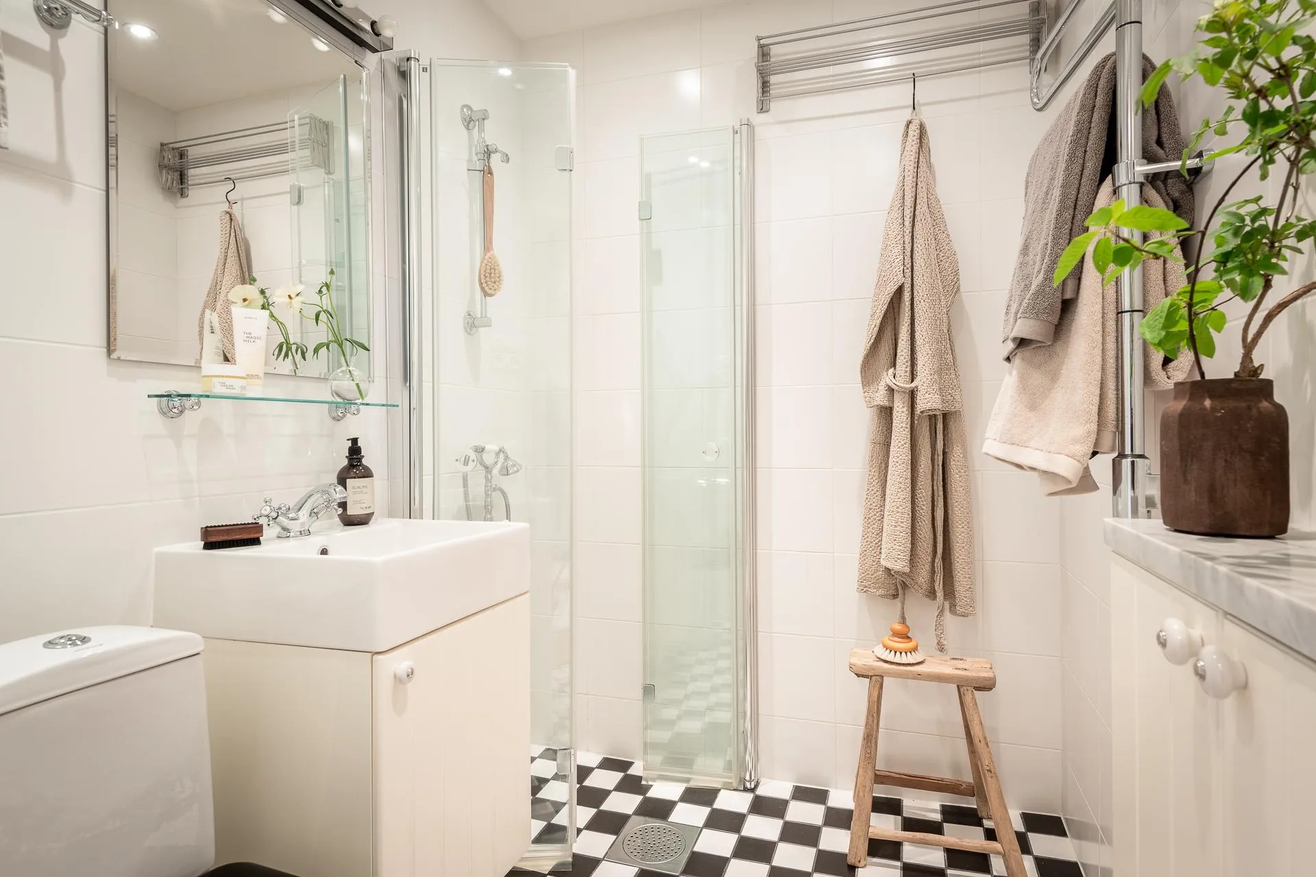 A minimalist bathroom with white tiled flooring, glass shower enclosure, and furniture.