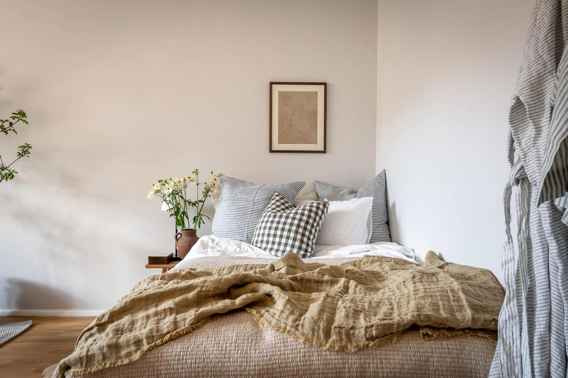 A minimalist bedroom featuring neutral textiles, a cozy armchair, and a warm wooden floor.