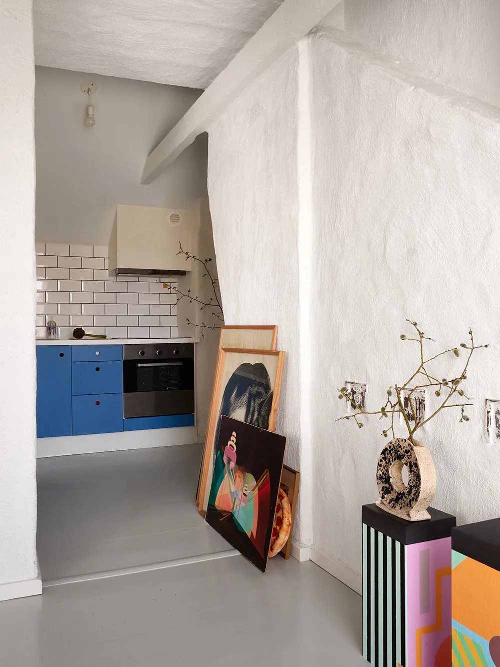 A modern kitchen with white painted walls, blue cabinets, and framed artwork leaning against the wall.