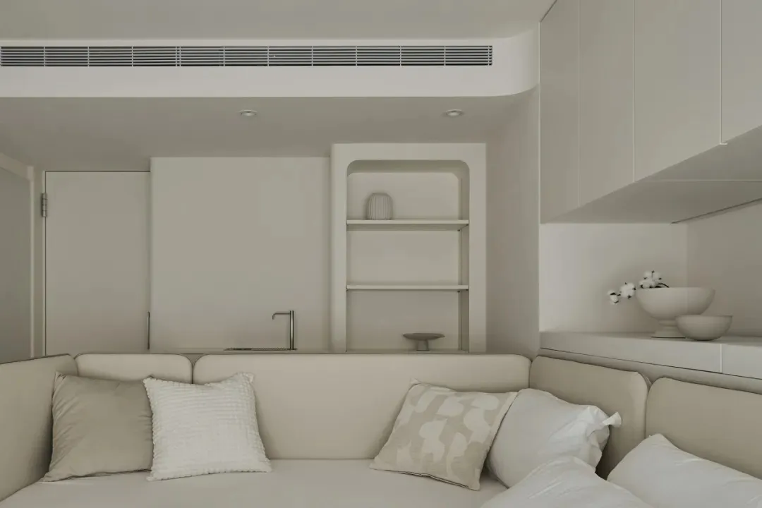 A minimalist living room with a white fabric couch, white cushions, and a white wall shelf.