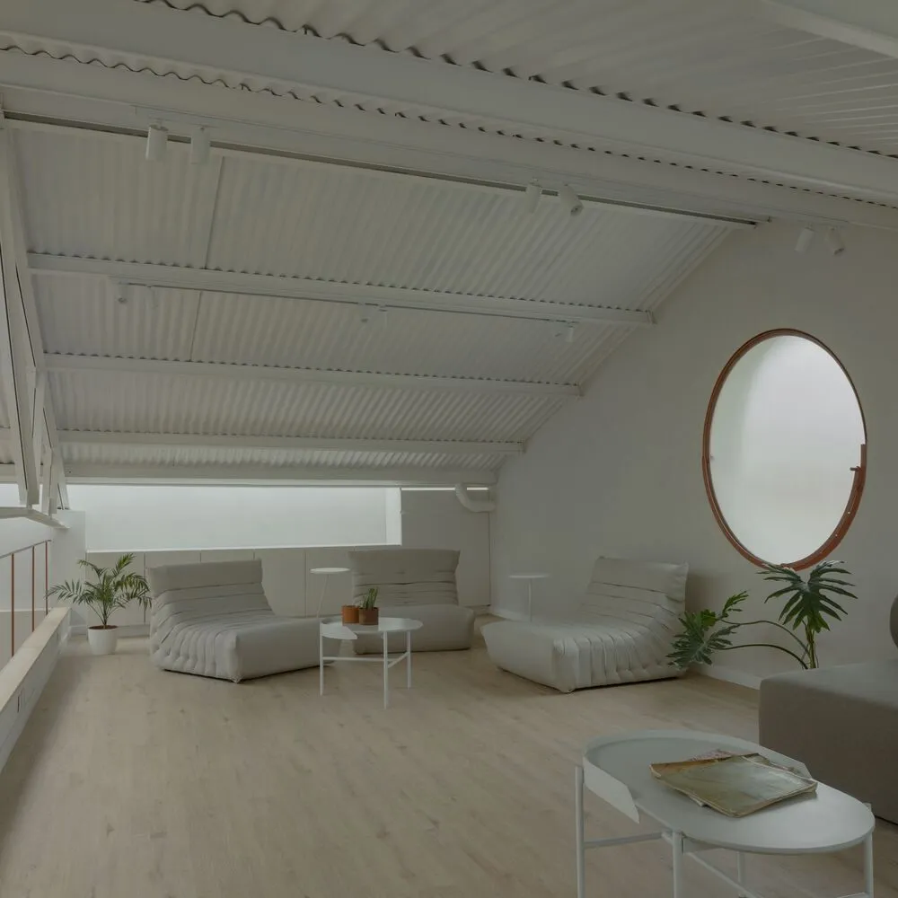 A minimalist living room with neutral-colored furniture and decor, featuring a large round window and a slanted ceiling.