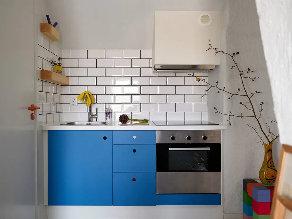 Modern minimalist kitchen with white tile backsplash, blue cabinets, and stainless steel appliances