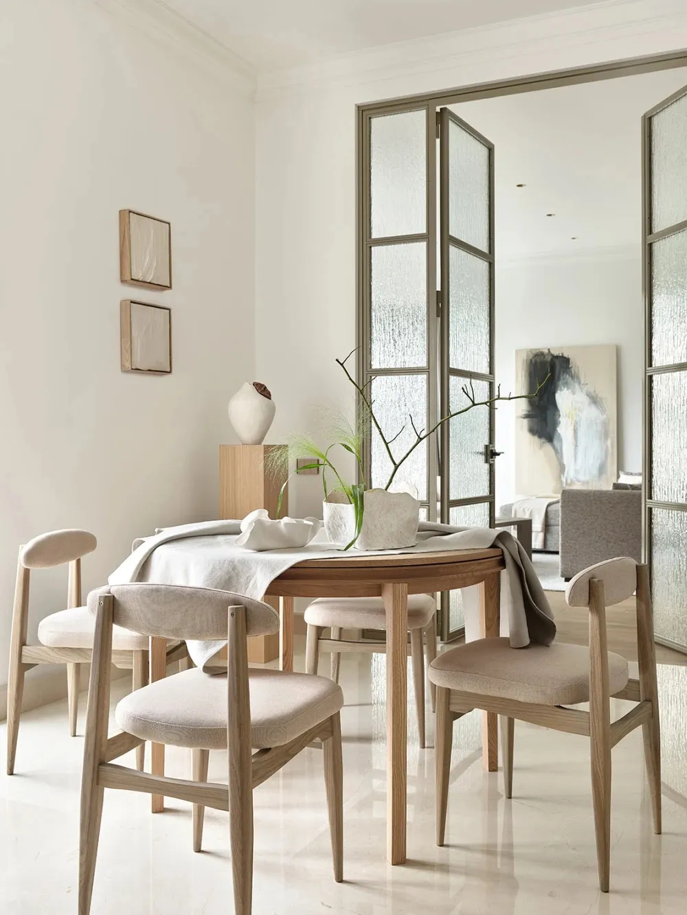 A modern dining room with solid wood furniture, white linens, and minimalist decor.
