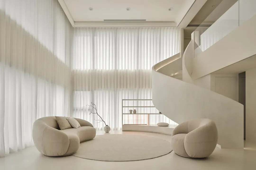 A modern living room with a minimalist design, featuring beige fabric seating and large windows with sheer curtains.