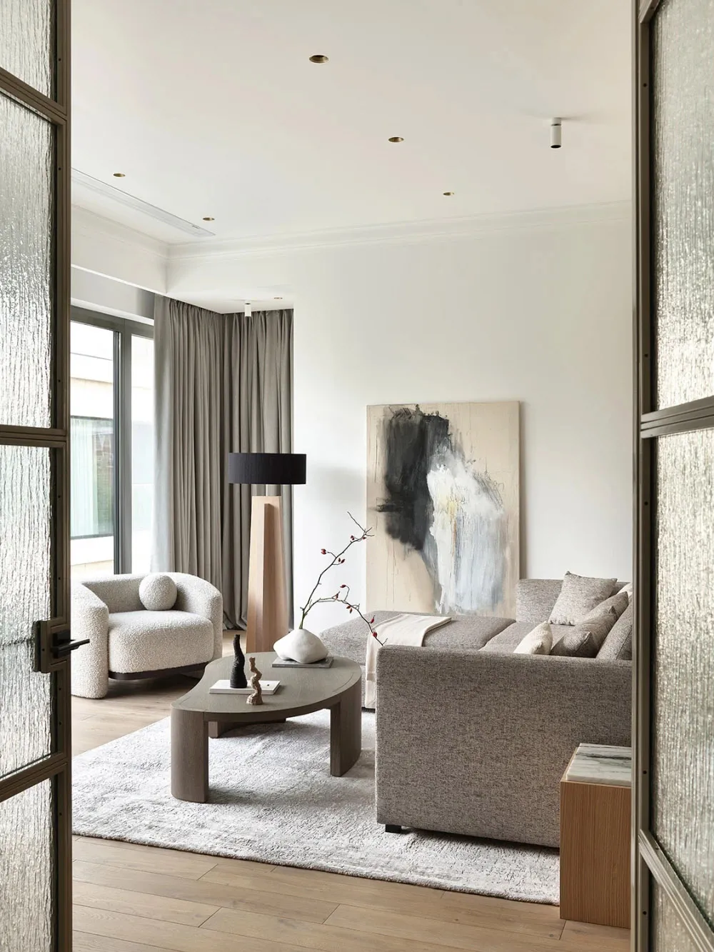 Modern living room with neutral-toned furniture, minimalist decor, and a large abstract painting.