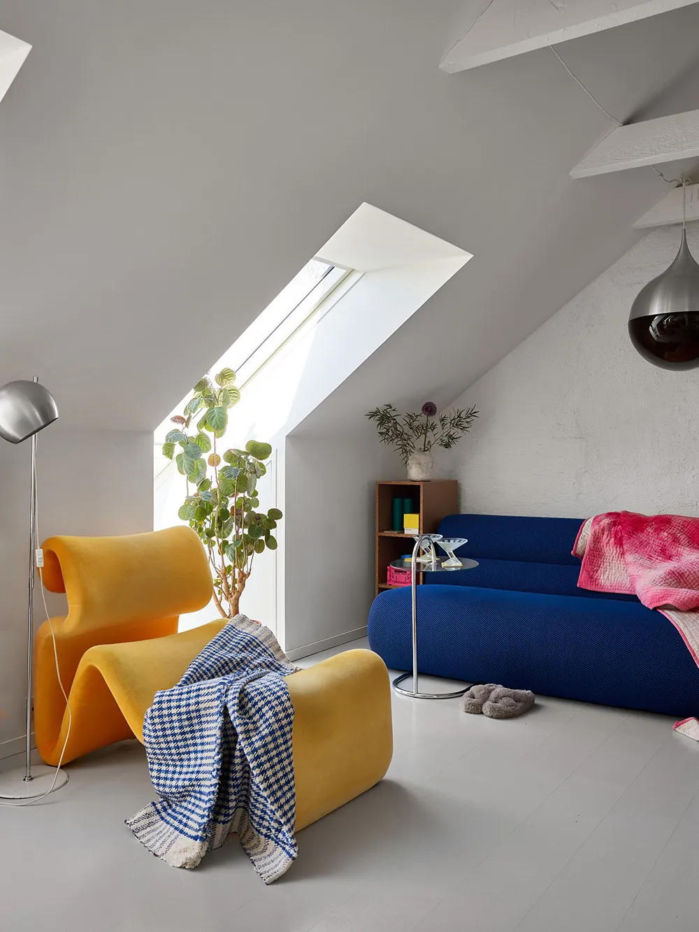 A minimalist living room with a yellow curved chair, blue sofa, and a skylight in the ceiling.