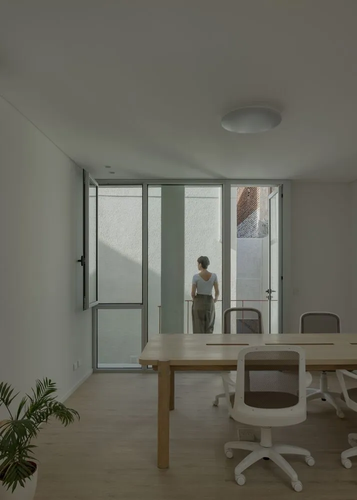 A modern office conference room with a wooden table and white office chairs.