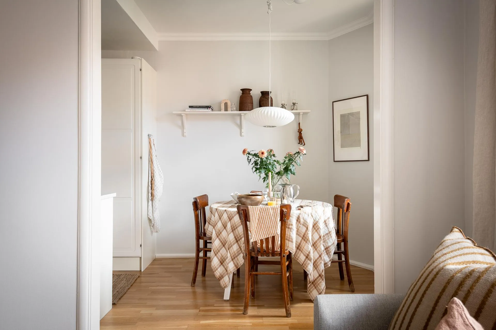 A cozy Scandinavian kitchen with a round wooden dining table, checkered tablecloth, and rustic decor.