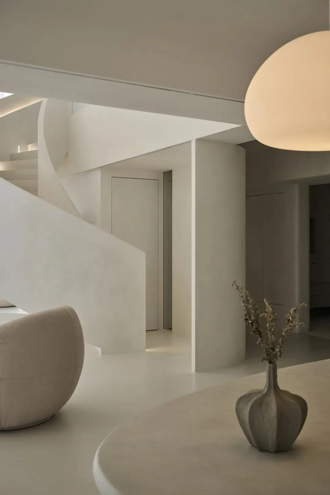 A minimalist living room with a concrete finish, featuring a large window with vertical blinds, a wavy white sofa, a matching