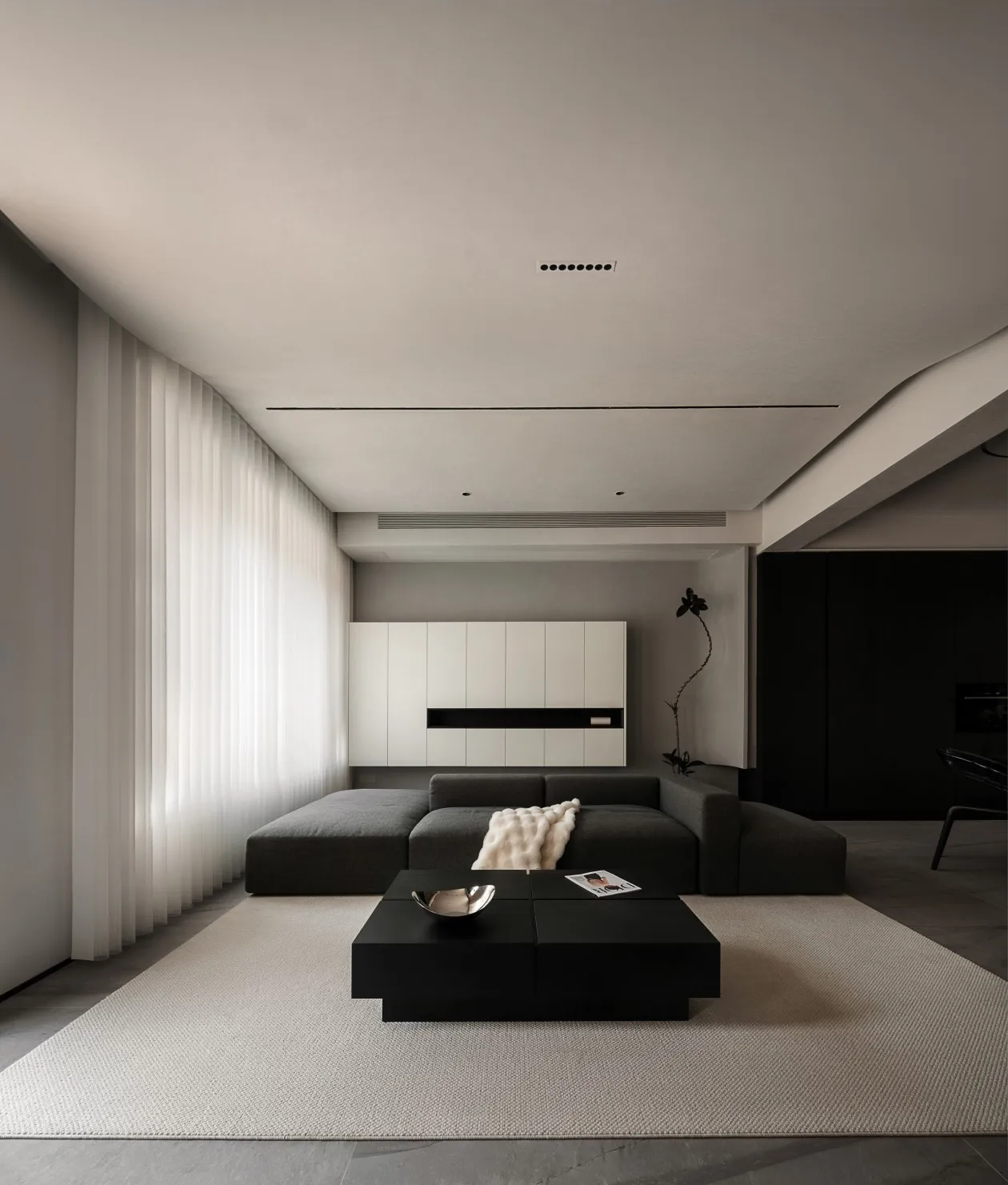 A minimalist living room with a fabric sofa, black coffee table, and white curtains.