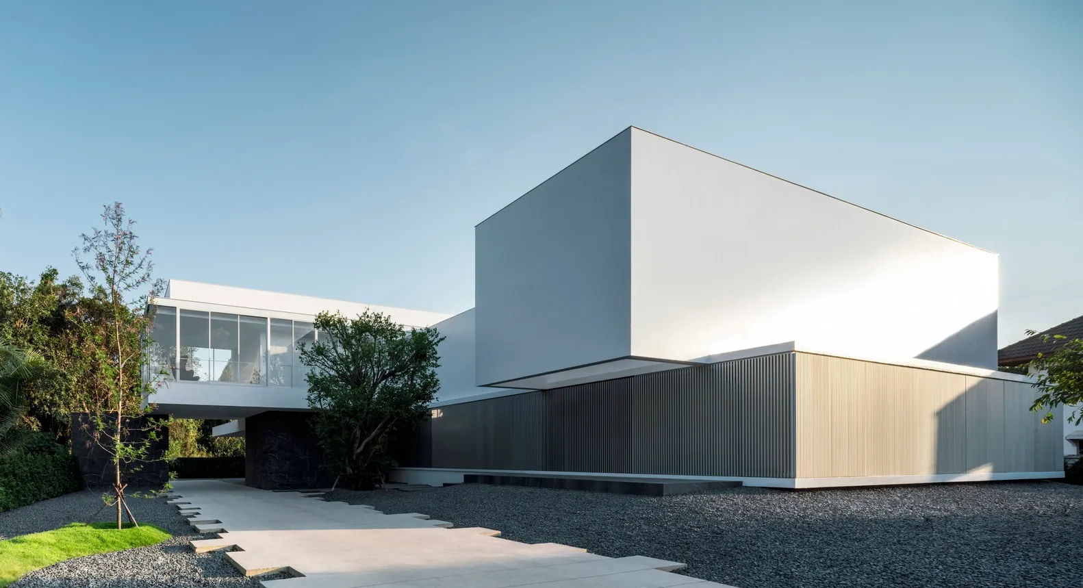 Modern minimalist white cube house with concrete exterior, glass windows, and a minimalist garden.