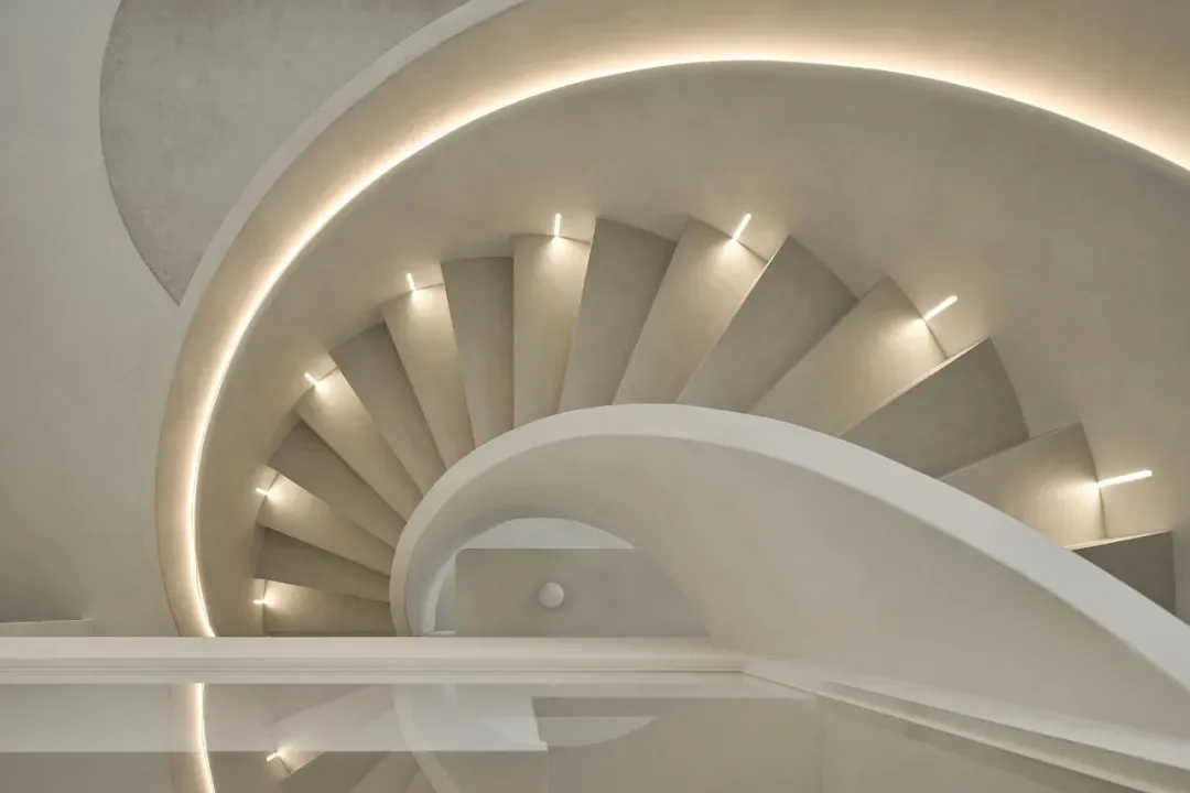 Circular modern staircase with concrete steps, illuminated by warm lighting fixtures.